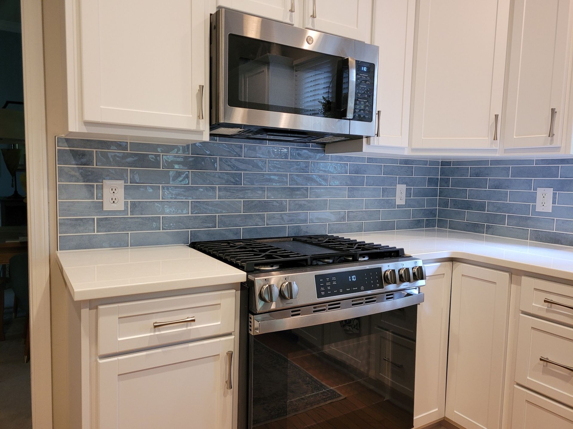 Blue glass subway tile backsplash installed behind a range in a white shaker kitchen