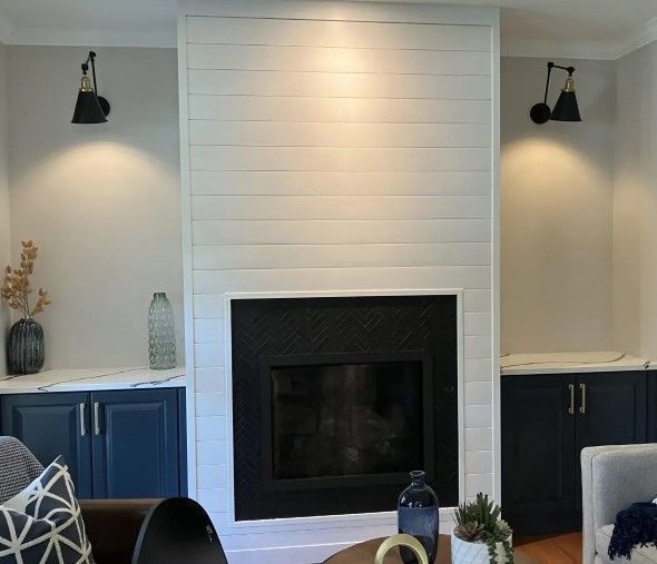 White shiplap fireplace chimney breast with a black herringbone firebox between navy blue built-in cabinets